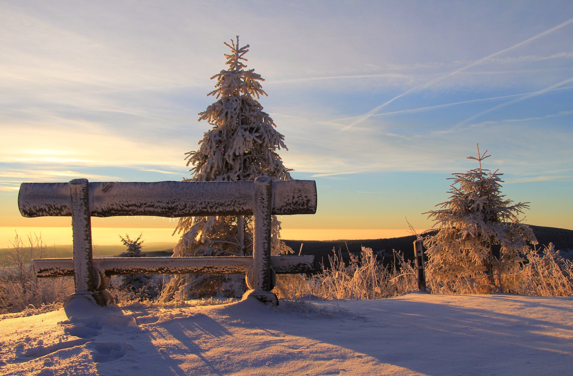 snow covered bench on mountain top during sunset