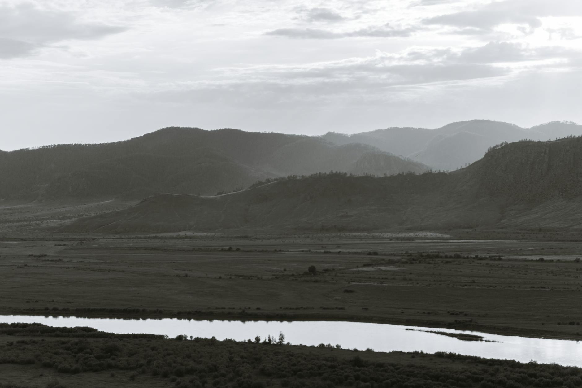 narrow river against mounts under cloudy sky