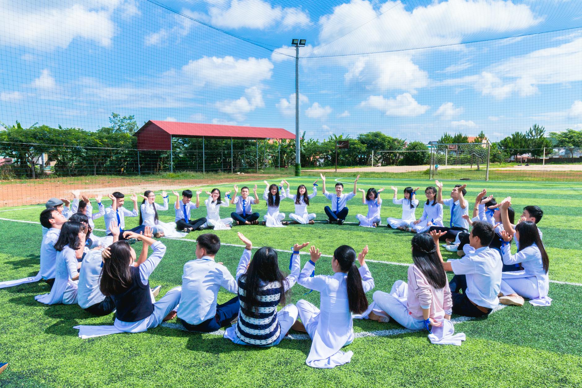 people sitting on green lawn grass while doing hands up at daytime